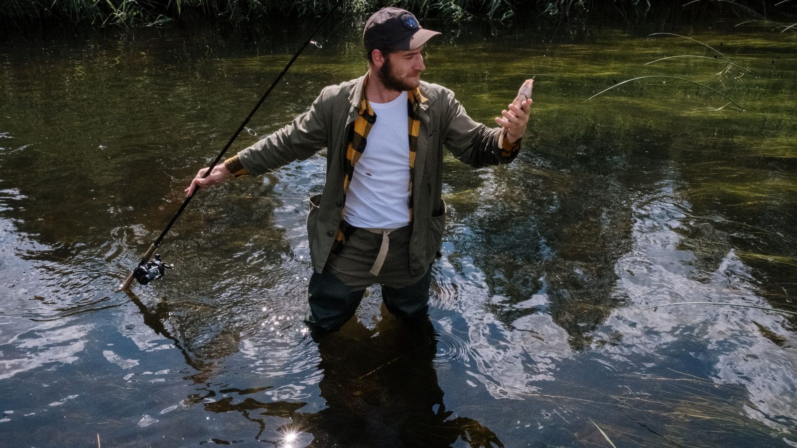 Pescador de agua dulce consultando un mapa en su teléfono junto a un lago